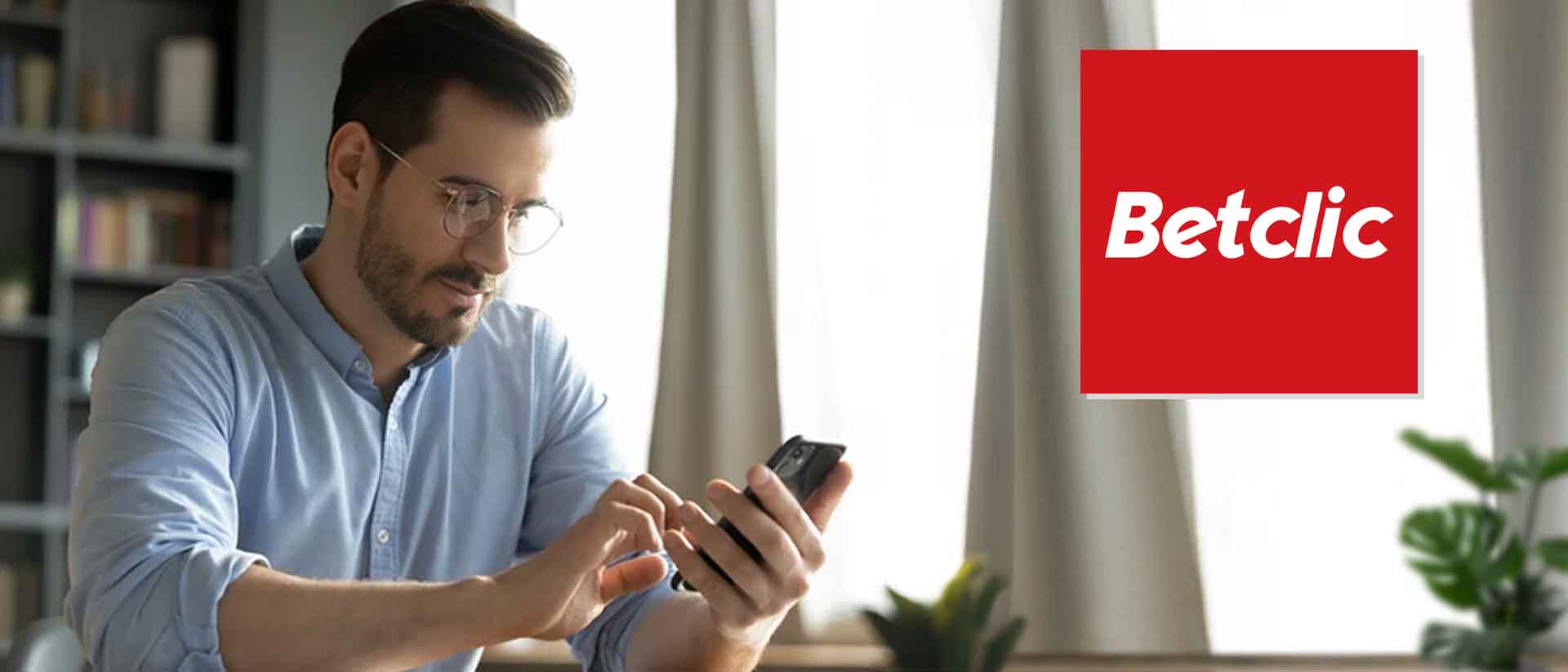 Imagem de homem segurando telemvel com logo da Betclic app colado ao lado direito em tons de branco e vermelho.