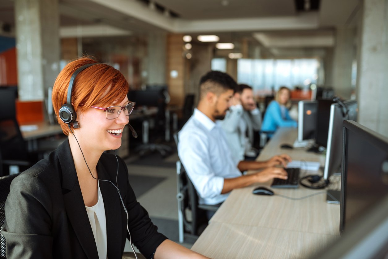 Imagem de funcionrios trabalhando lado a lado em um escritrio com rapariga de cabelo ruivo sorrindo em evidncia.